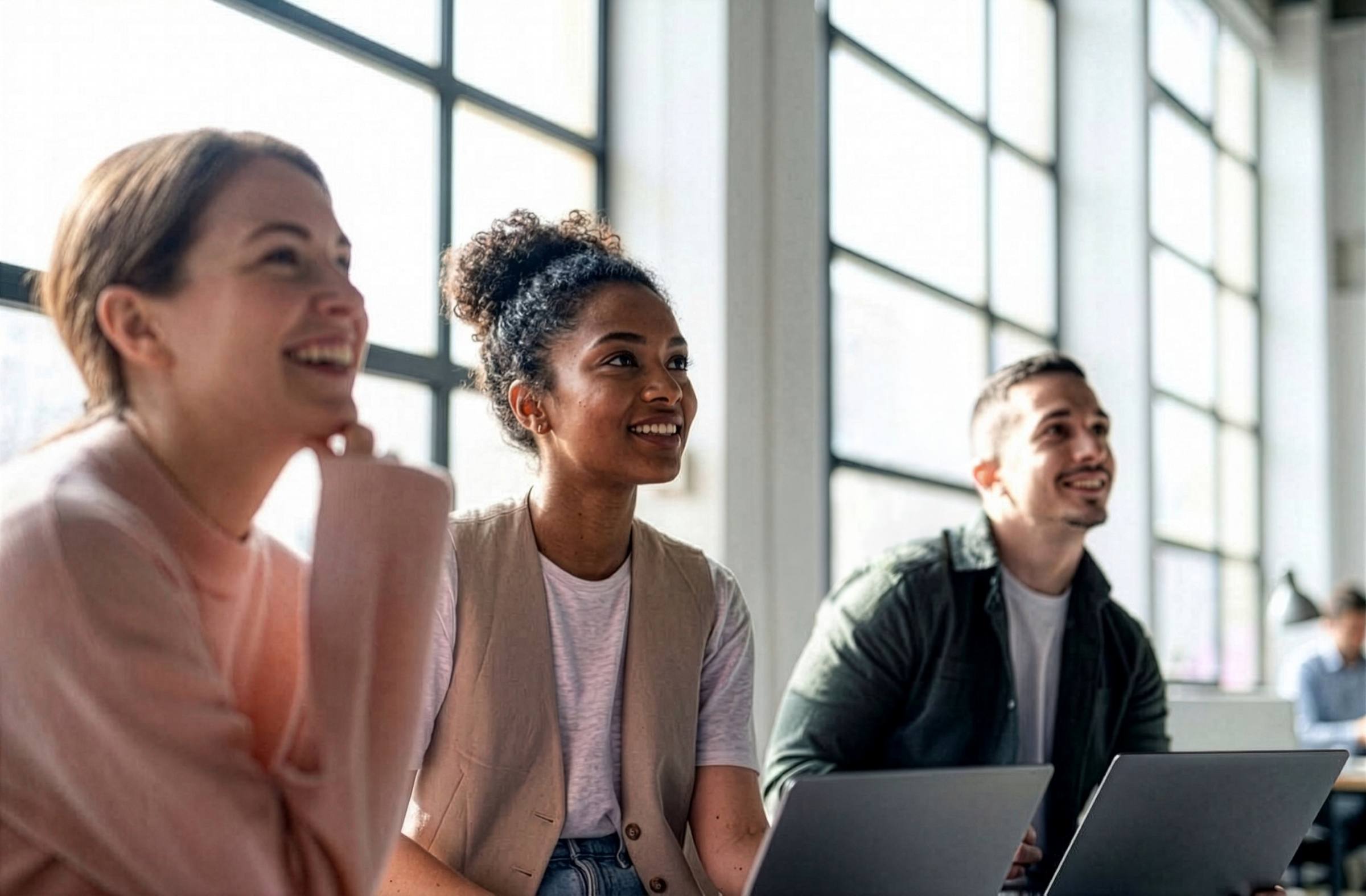 Three colleagues smiling as they look up during a meeting